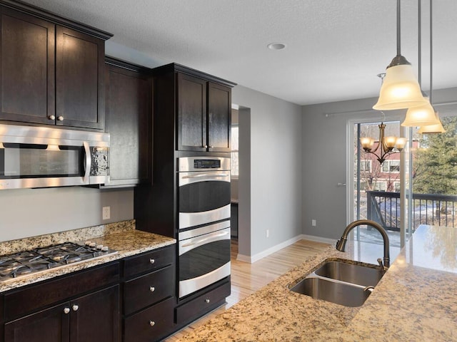 kitchen featuring sink, hanging light fixtures, dark brown cabinets, stainless steel appliances, and light stone counters