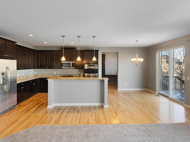 kitchen featuring a kitchen island with sink, light stone countertops, decorative light fixtures, and stainless steel appliances