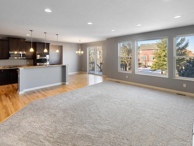 kitchen with decorative light fixtures, a chandelier, light stone counters, dark brown cabinetry, and stainless steel appliances