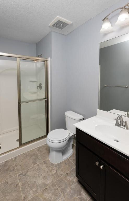 bathroom with vanity, toilet, a shower with door, and a textured ceiling