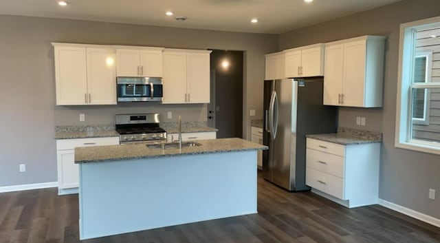 kitchen with stainless steel appliances, sink, white cabinetry, and an island with sink