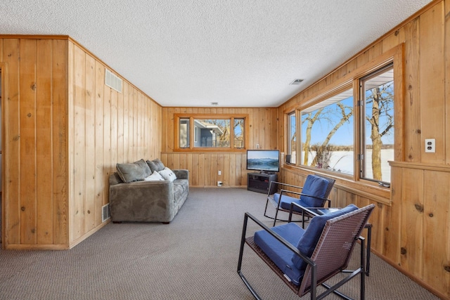 living room featuring light colored carpet, wooden walls, and a textured ceiling