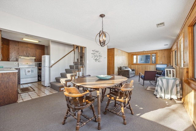 dining space with sink, wood walls, a textured ceiling, a notable chandelier, and light colored carpet