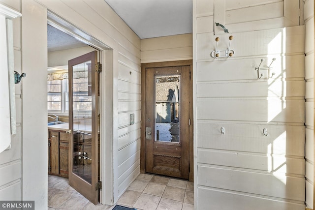 doorway to outside with wood walls and light tile patterned flooring