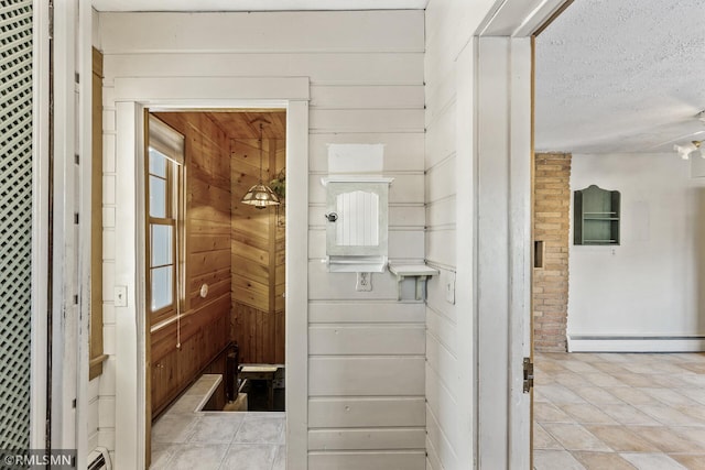 hallway featuring baseboard heating, wooden walls, and a textured ceiling