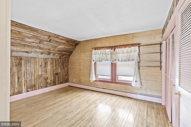 additional living space featuring wooden walls, baseboard heating, a textured ceiling, wood-type flooring, and vaulted ceiling