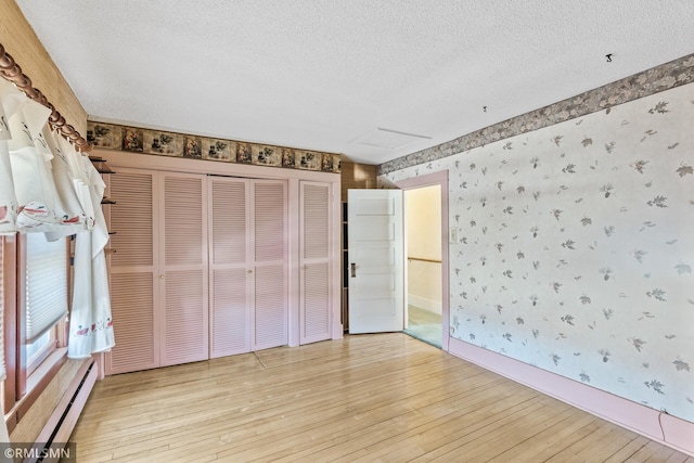 unfurnished bedroom featuring light wood-type flooring, a baseboard heating unit, a closet, and a textured ceiling