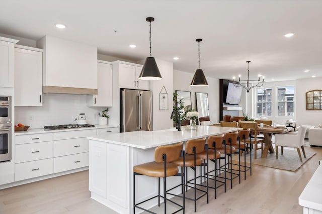 kitchen with appliances with stainless steel finishes, decorative light fixtures, white cabinetry, an island with sink, and a breakfast bar area