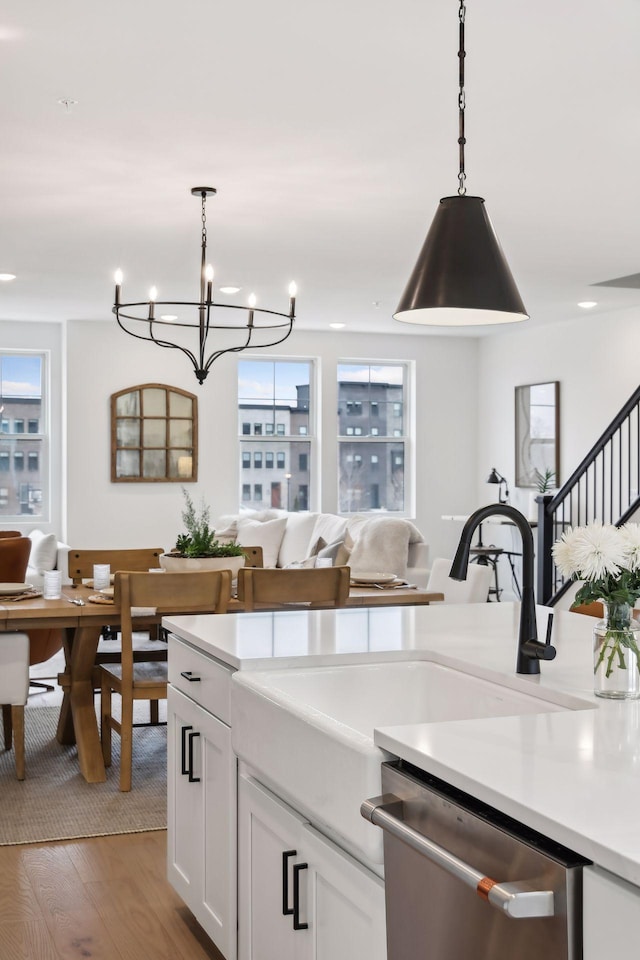 kitchen with white cabinetry, decorative light fixtures, stainless steel dishwasher, a notable chandelier, and hardwood / wood-style floors