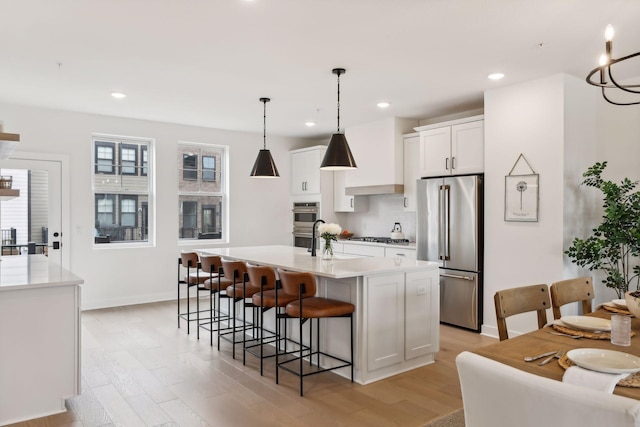 kitchen with a breakfast bar area, white cabinets, light hardwood / wood-style floors, stainless steel appliances, and a center island with sink