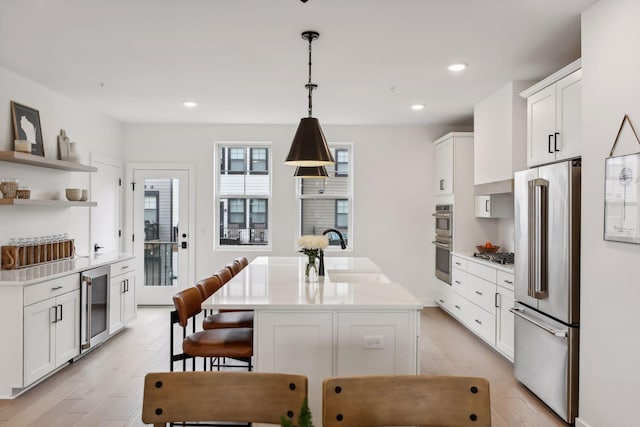 kitchen featuring wine cooler, sink, appliances with stainless steel finishes, an island with sink, and pendant lighting