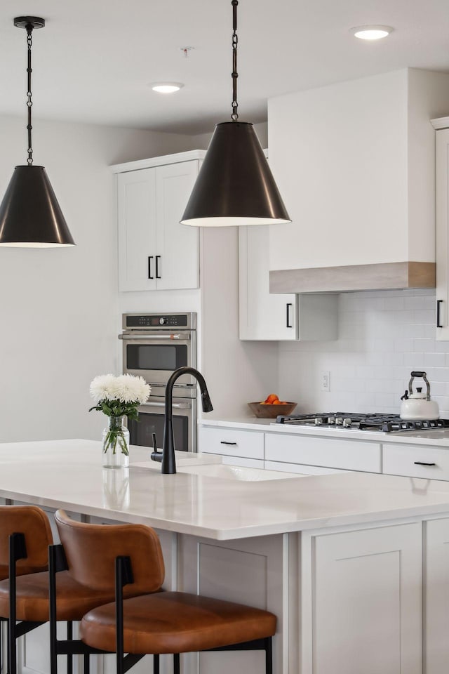 kitchen with appliances with stainless steel finishes, hanging light fixtures, backsplash, a kitchen breakfast bar, and white cabinets