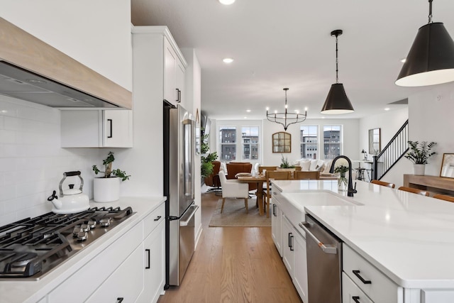 kitchen featuring light wood-style flooring, wall chimney range hood, appliances with stainless steel finishes, a sink, and light countertops