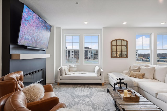 living area featuring baseboards, a glass covered fireplace, and a wealth of natural light