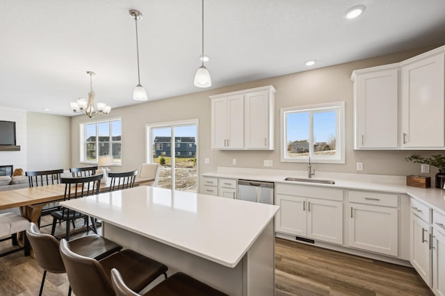 kitchen with decorative light fixtures, dark hardwood / wood-style flooring, stainless steel dishwasher, white cabinets, and sink