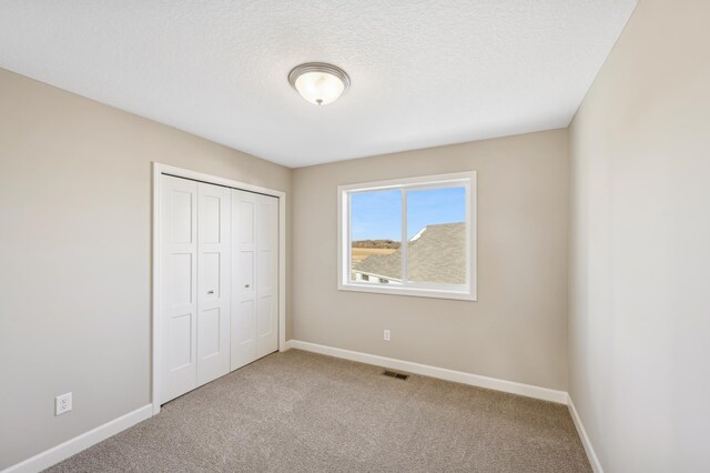 unfurnished bedroom with a textured ceiling, a closet, and light colored carpet