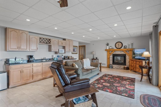 living room with ceiling fan, sink, a drop ceiling, and a fireplace