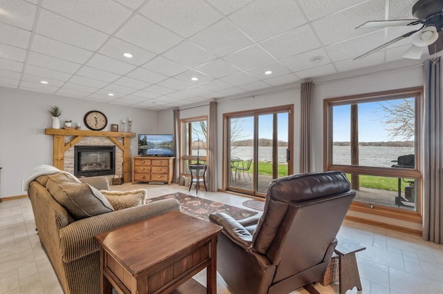 living room featuring ceiling fan, a paneled ceiling, and a fireplace