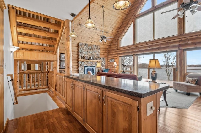 kitchen featuring dark hardwood / wood-style floors, rustic walls, hanging light fixtures, a stone fireplace, and high vaulted ceiling