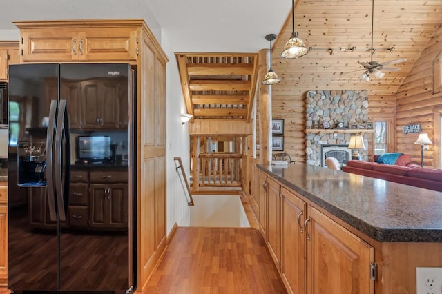 kitchen with log walls, decorative light fixtures, a stone fireplace, light hardwood / wood-style floors, and black fridge