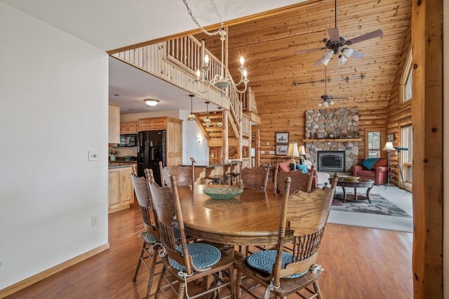 dining room featuring a high ceiling, ceiling fan with notable chandelier, a fireplace, and light hardwood / wood-style flooring