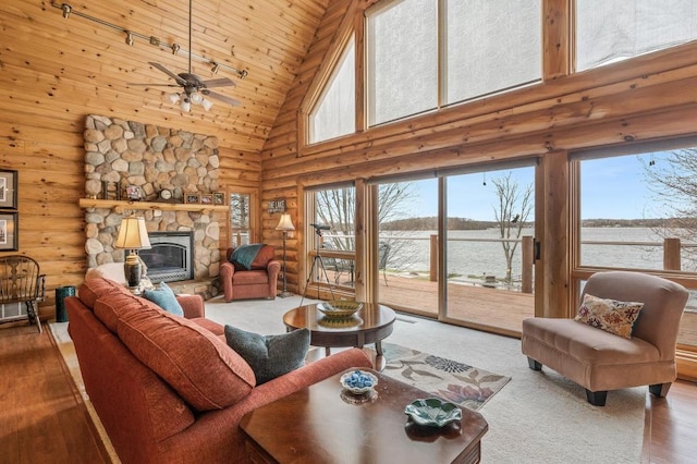 living room with log walls, wood-type flooring, a fireplace, ceiling fan, and high vaulted ceiling