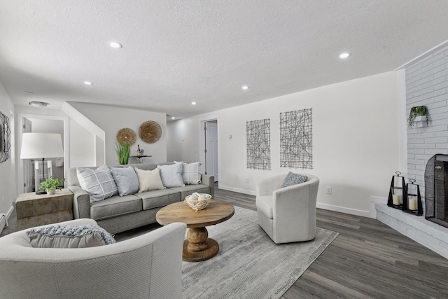 living room with a textured ceiling, a brick fireplace, and dark hardwood / wood-style floors