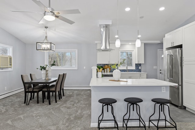 kitchen featuring island range hood, high end fridge, backsplash, decorative light fixtures, and white cabinets