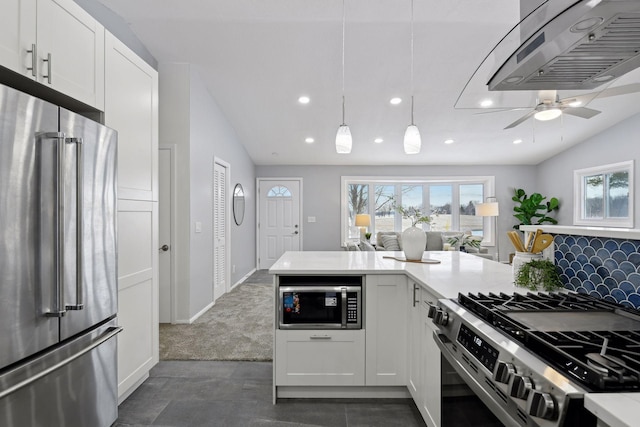 kitchen with appliances with stainless steel finishes, decorative light fixtures, white cabinetry, wall chimney range hood, and dark carpet