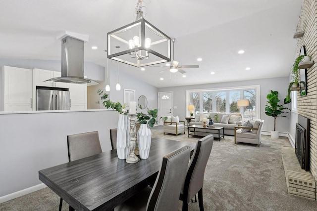 dining room with ceiling fan with notable chandelier, a fireplace, vaulted ceiling, and carpet