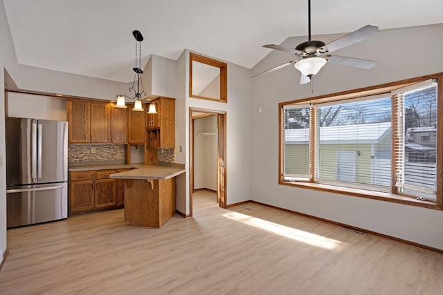 kitchen featuring lofted ceiling, decorative light fixtures, decorative backsplash, a kitchen breakfast bar, and stainless steel fridge