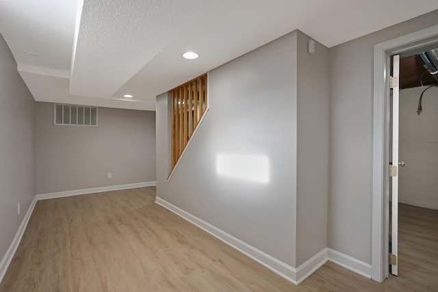 basement featuring a textured ceiling and light hardwood / wood-style flooring