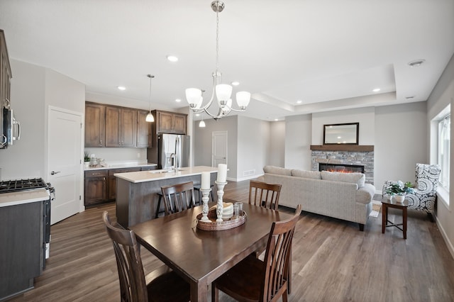 dining space featuring an inviting chandelier, a fireplace, dark hardwood / wood-style flooring, and a tray ceiling