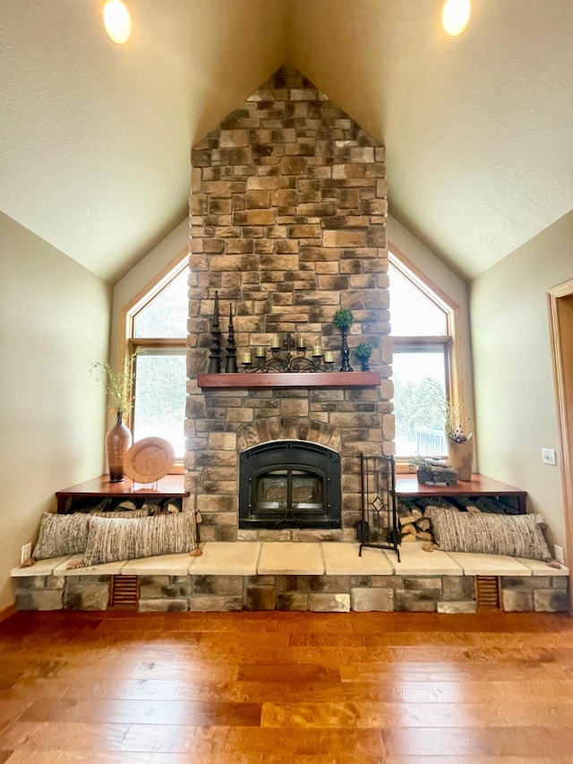 living room featuring vaulted ceiling, a stone fireplace, and wood-type flooring