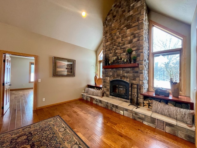 living room with high vaulted ceiling, a stone fireplace, and hardwood / wood-style floors