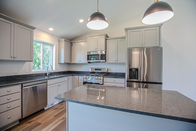 kitchen with vaulted ceiling, stainless steel appliances, hanging light fixtures, and dark stone counters