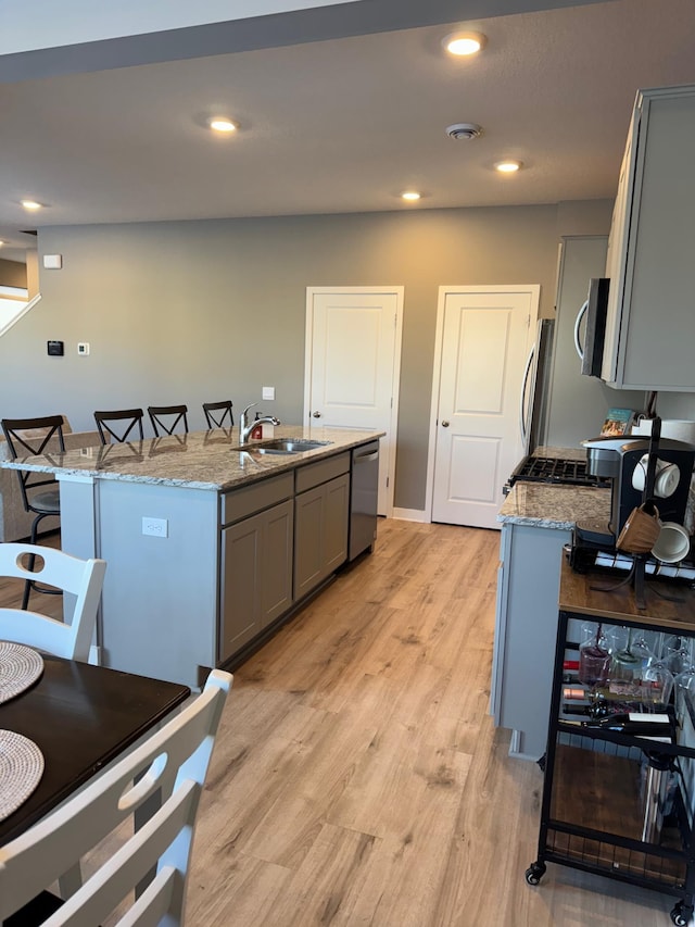 kitchen with light stone countertops, appliances with stainless steel finishes, a center island with sink, and sink