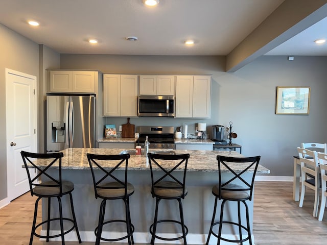 kitchen featuring white cabinets, stainless steel appliances, light wood-type flooring, light stone counters, and a breakfast bar area