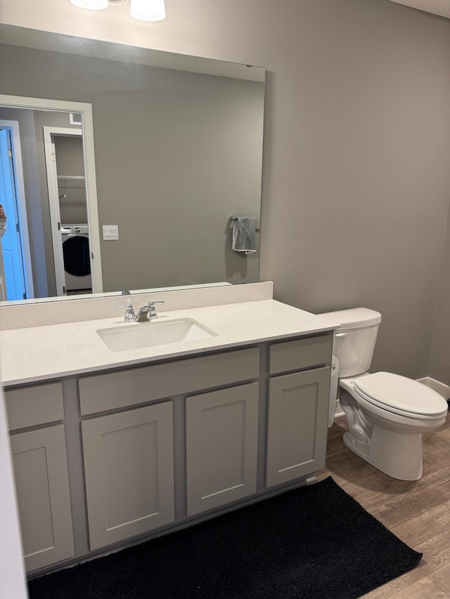 bathroom featuring toilet, vanity, washer / dryer, and hardwood / wood-style flooring