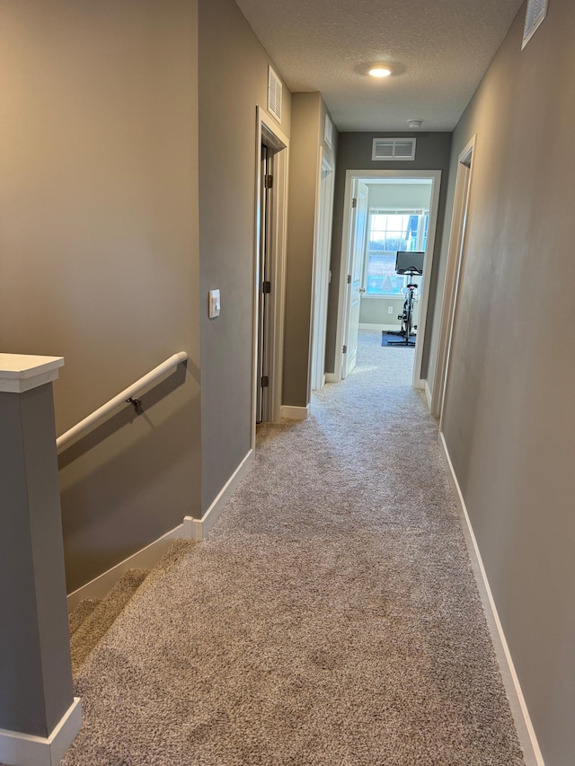 corridor with a textured ceiling and light colored carpet