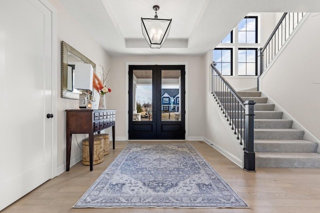 entrance foyer with an inviting chandelier, light hardwood / wood-style floors, a raised ceiling, and french doors