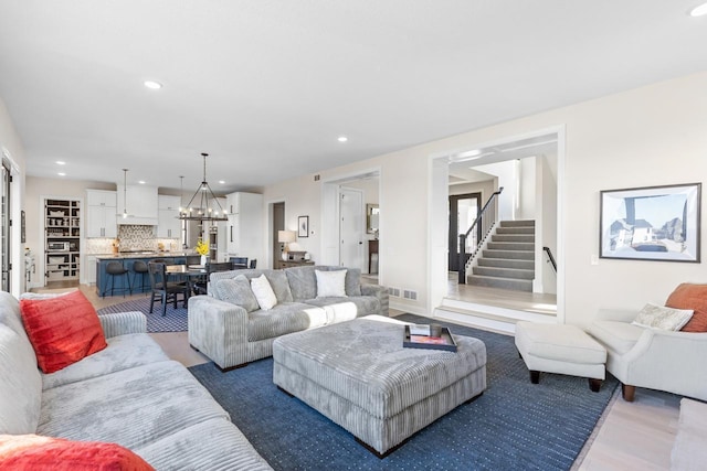 living room with light wood-style flooring, recessed lighting, visible vents, stairs, and an inviting chandelier