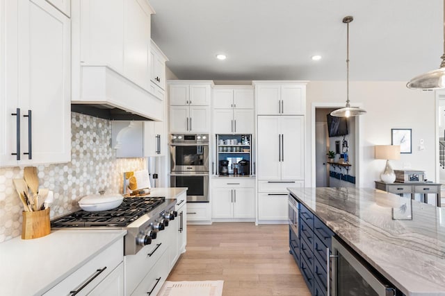 kitchen featuring white cabinetry, appliances with stainless steel finishes, light wood finished floors, decorative light fixtures, and tasteful backsplash