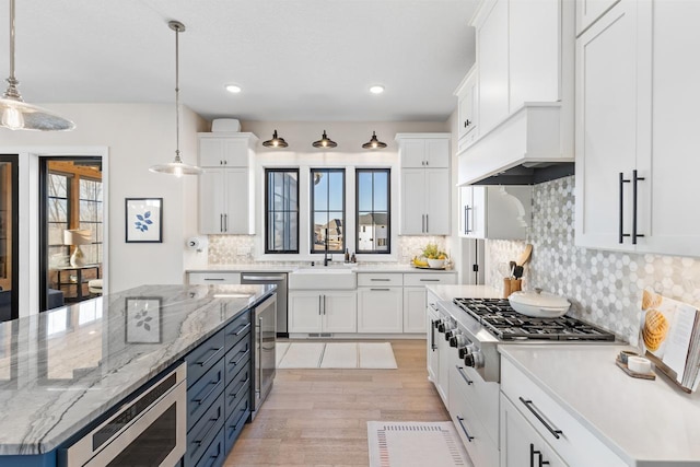 kitchen featuring pendant lighting, stainless steel appliances, light wood-style floors, white cabinets, and a sink