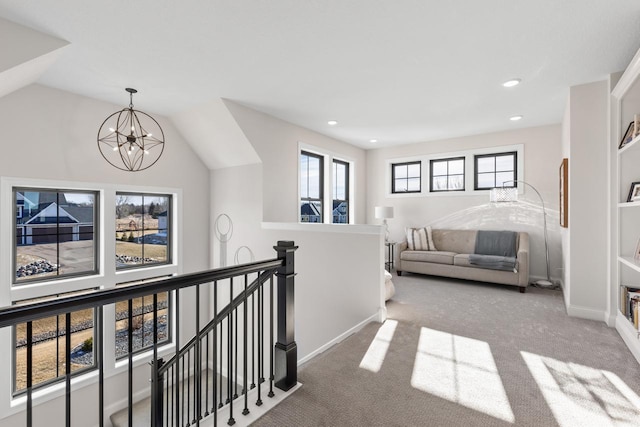 hall featuring carpet floors, an upstairs landing, baseboards, vaulted ceiling, and an inviting chandelier