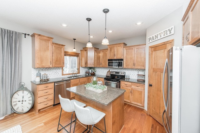 kitchen featuring stainless steel appliances, a kitchen breakfast bar, hanging light fixtures, a kitchen island, and sink