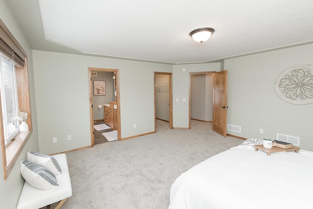 carpeted bedroom featuring ensuite bath, a walk in closet, a closet, and a textured ceiling