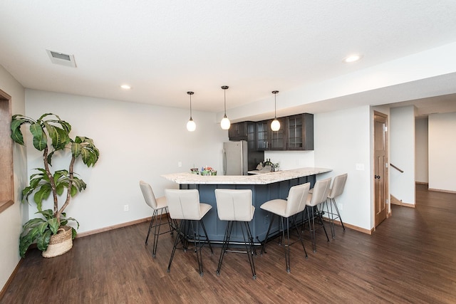 kitchen with a kitchen bar, dark wood-type flooring, stainless steel fridge, and kitchen peninsula