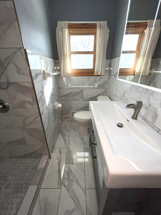 bathroom with a healthy amount of sunlight, tile walls, vanity, and tiled shower