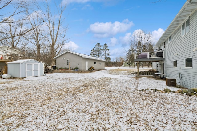 snowy yard featuring a deck, central air condition unit, and a shed